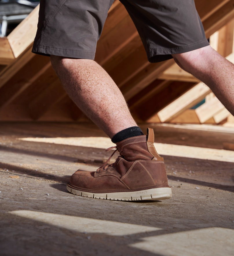 Waist down shot of man in gray shorts wearing brown San Jose soft toe boots and standing in front of wood project. 