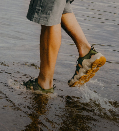 A person wearing a pair of KEEN sandals, stepping through water.