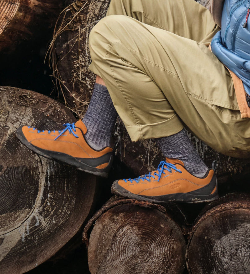 Waist-down shot of man sitting on wooden logs while wearing orange Jasper sneakers and tan pants.