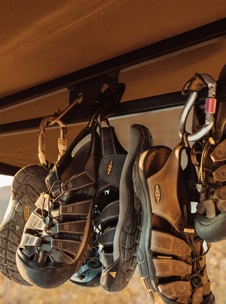 three pairs of newport sandals hanging from van room attached with carabiner 