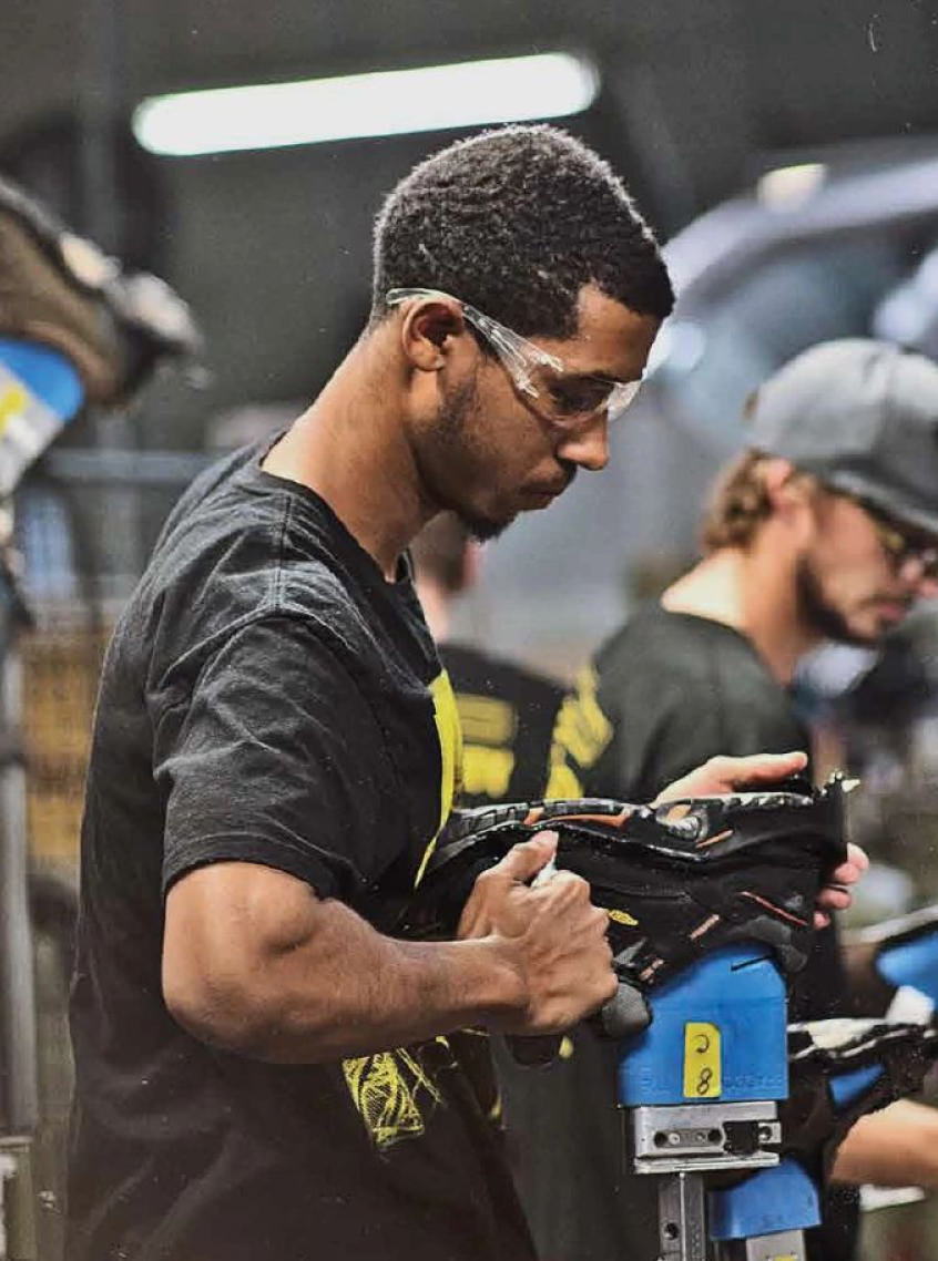 A man wearing safety glasses using machinery to mold a shoe 