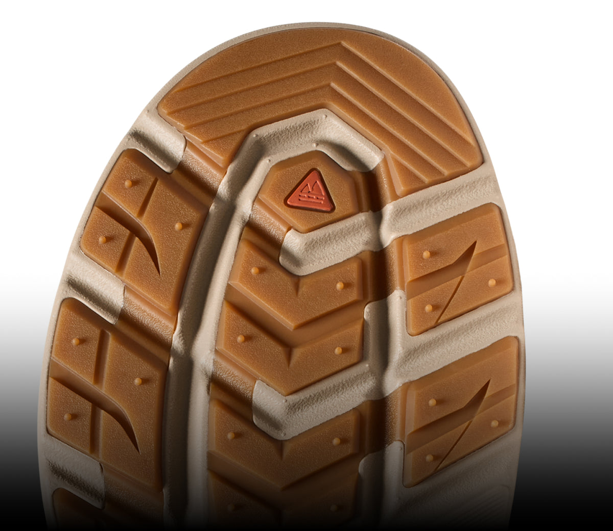 Close-up of a rugged tan shoe outsole with a triangular orange logo and aggressive traction lugs.