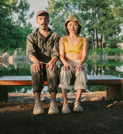 Man and woman sitting on park bench in front of pond while wearing monochrome Newport sandals. 