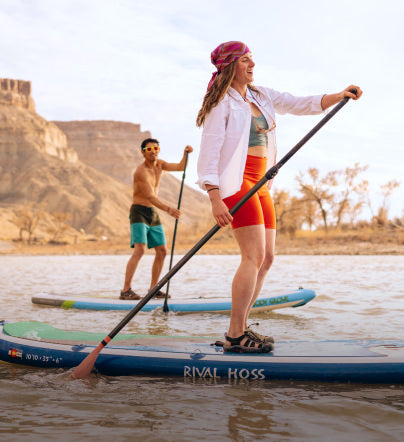Man and woman on stand up paddle boatds paddling through desert river while wearing Newports. 