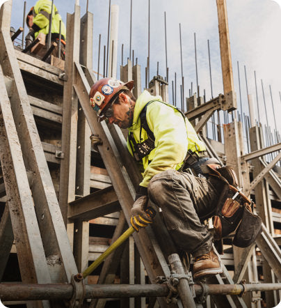 Man in construction gear working on frame of builing with handheld tools.