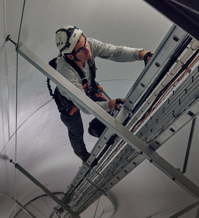 Man in safety helmet and harness climbing a ladder within the interior of a wind turbine