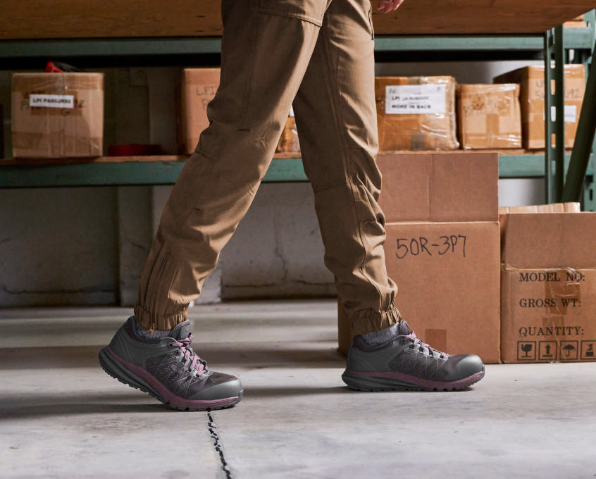 Kneew down view of woman wearing Vista Energy ESD work shoes and walking in front of boxes