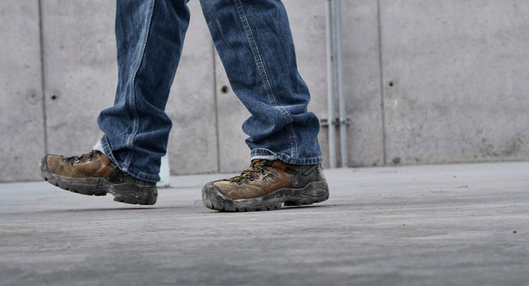 Knee down view of man wearing Pittsburgh energy boots and jeans walking on cement 