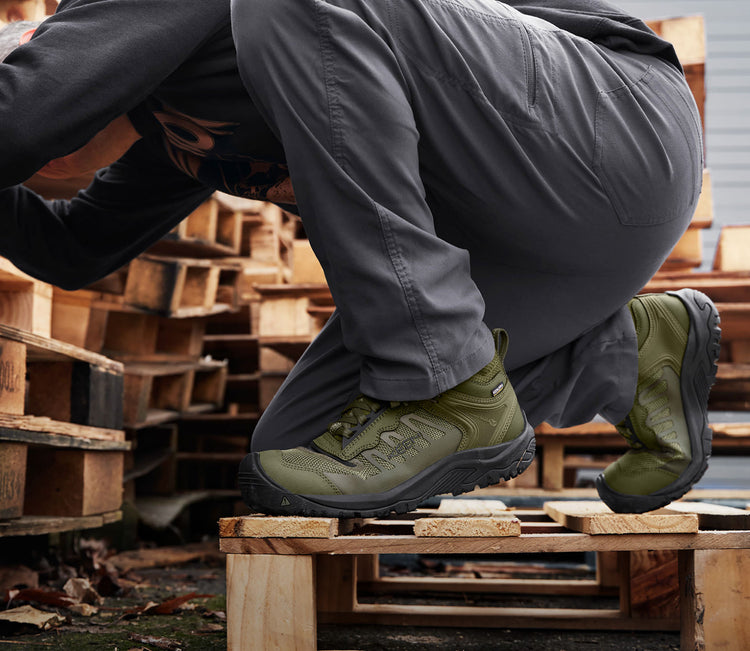 Man crouching down on wooden palette whearing green Reno work shoes