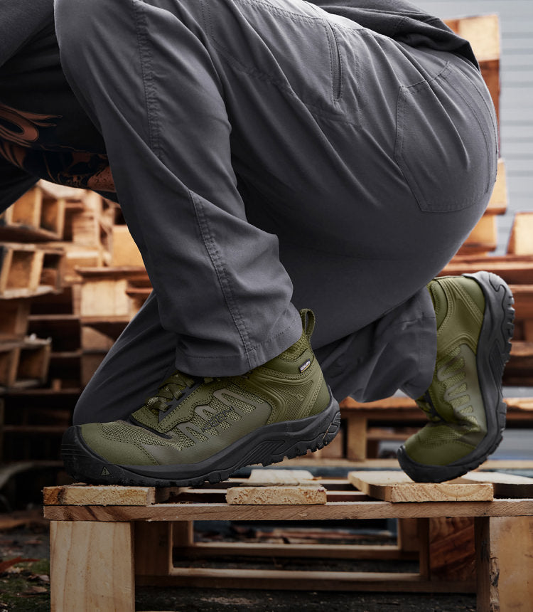 Man crouching down on wooden palette whearing green Reno work shoes
