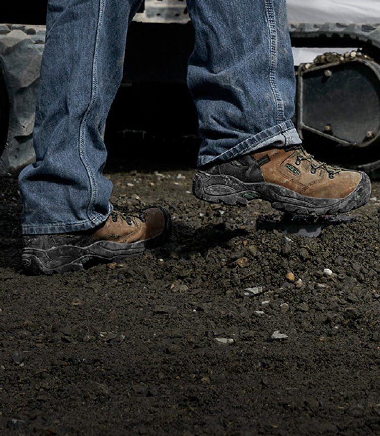 Knee down view of man wearing Pittsburgh energy boots walking through mud