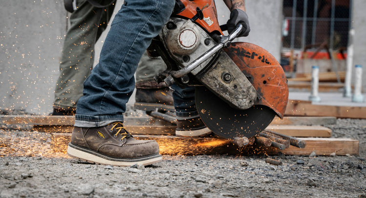 Knee down view of man wearing Cincinnati work boots and using a circular saw to cut metal 