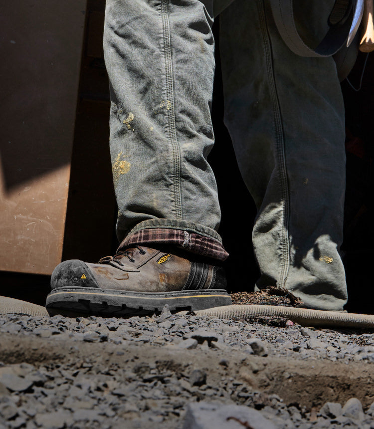 Knee down view of man wearing Abitibi II on gravel, muddy terrain.