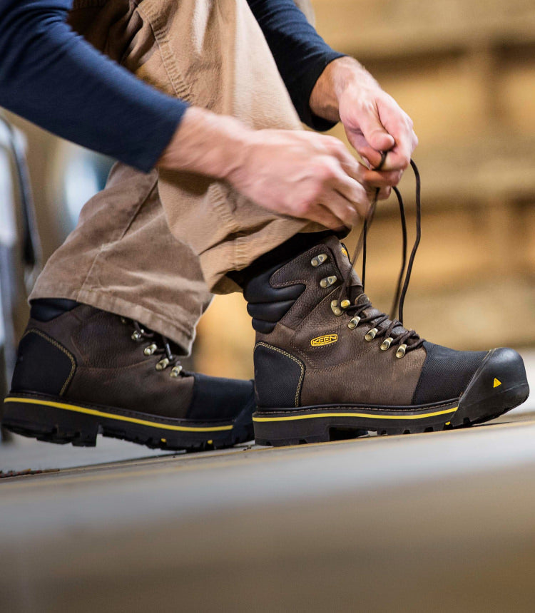 Knee down view of man lacing up Milwaukee work boots in warehouse