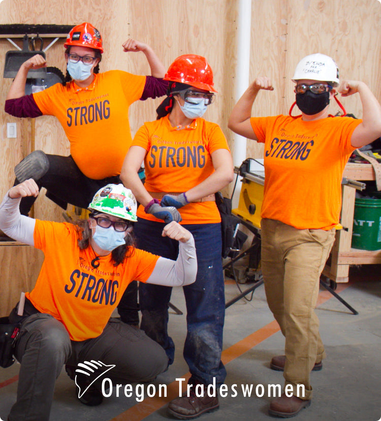 Four women wearing safety helmets and bright orange shirts that say"strong" on them flexing and posing 