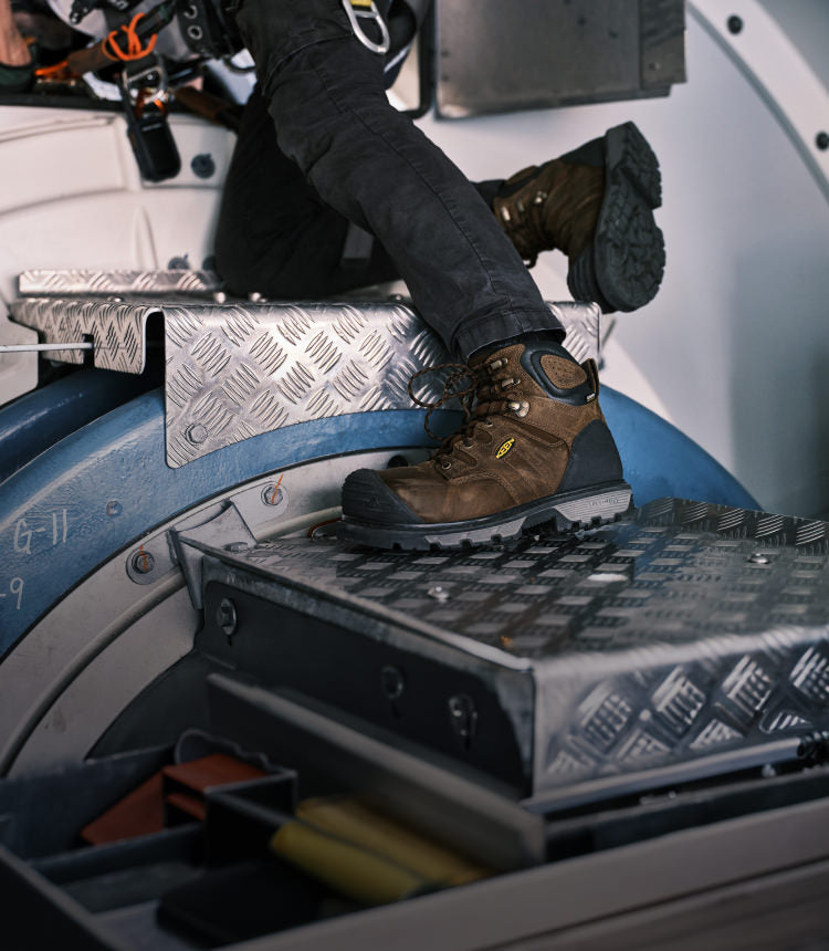 Waist down shot of a man in jeans and safety harness wearing Camden work boots and working on a metal structure 