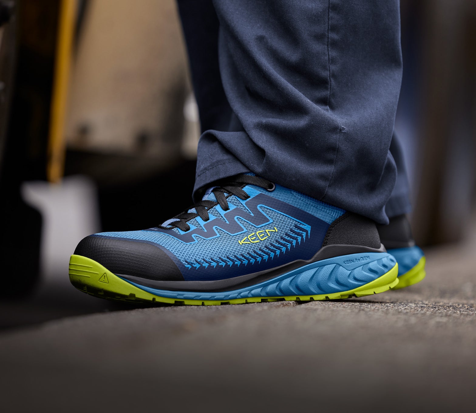 Knee-down shot of man wearing blue and green Arvada work shoes and standing on cement