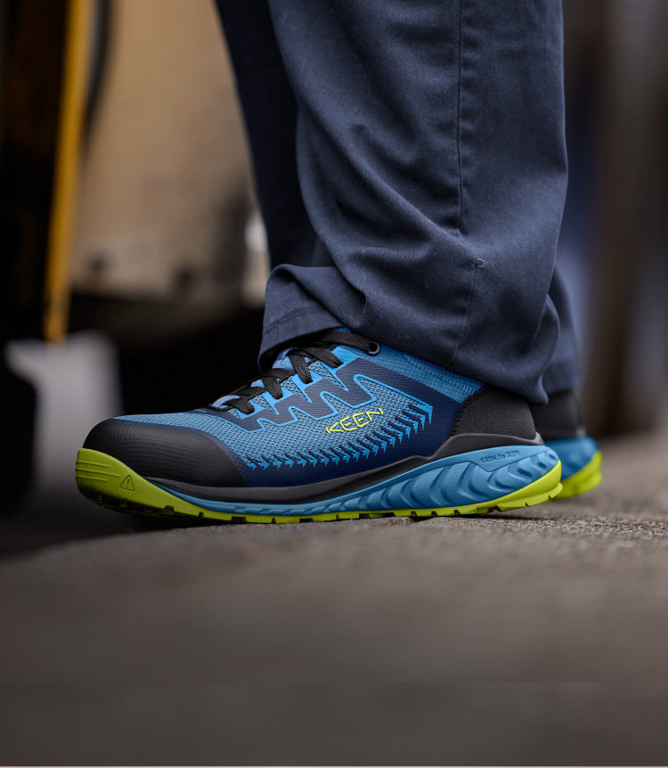 Knee-down shot of man wearing blue and green Arvada work shoes and standing on cement
