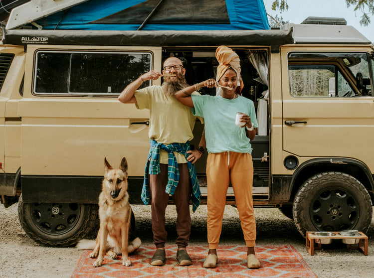 Man, Woman, and dog in front of van brushing their teeth and standing on a rug