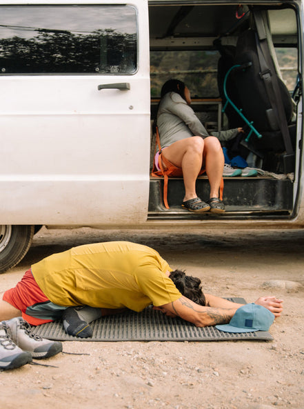 Man doing yoga on mat in front of van in dirt parking lot