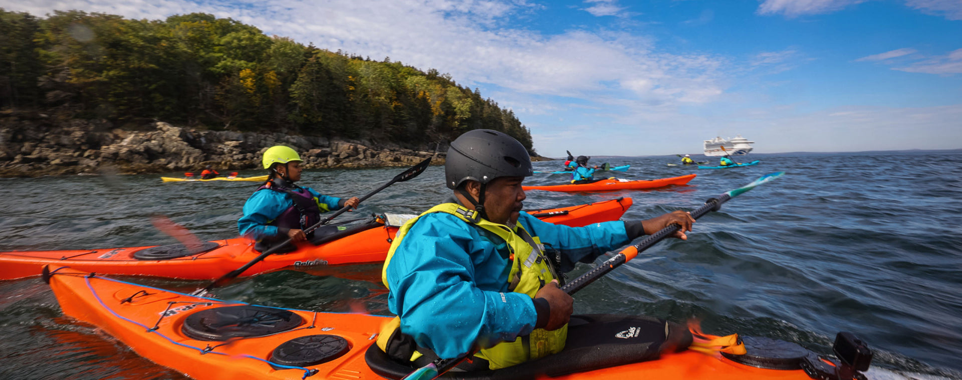 Group of ocean kayakers paddling along foresty and rocky coastline