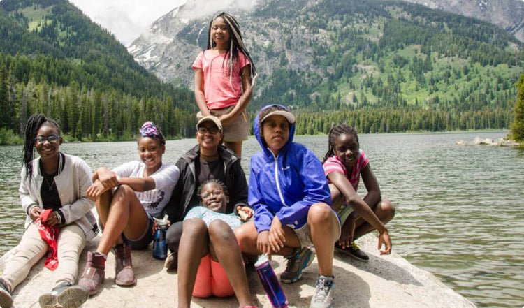 Group of kids posing on lakefront rock with mountains and fog in the back. 