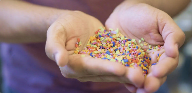 Close-up of hands holdling extremely small, multicolored flakes of rubber material