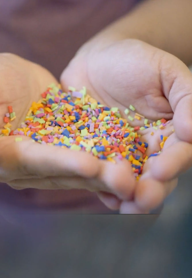 Close-up of hands holdling extremely small, multicolored flakes of rubber material