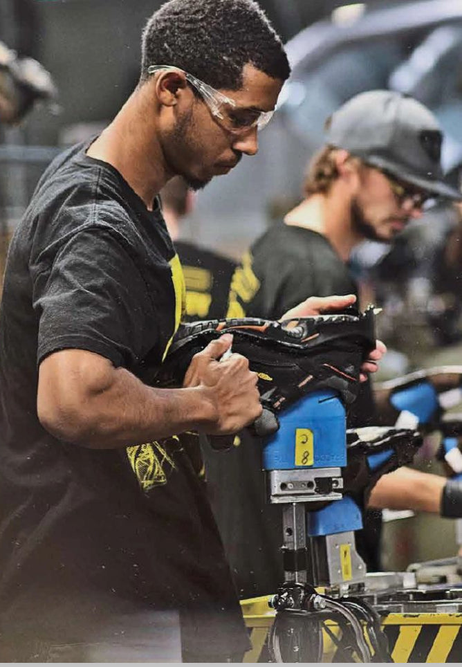 Man using blue handheld machine to mold a shoe in a factory