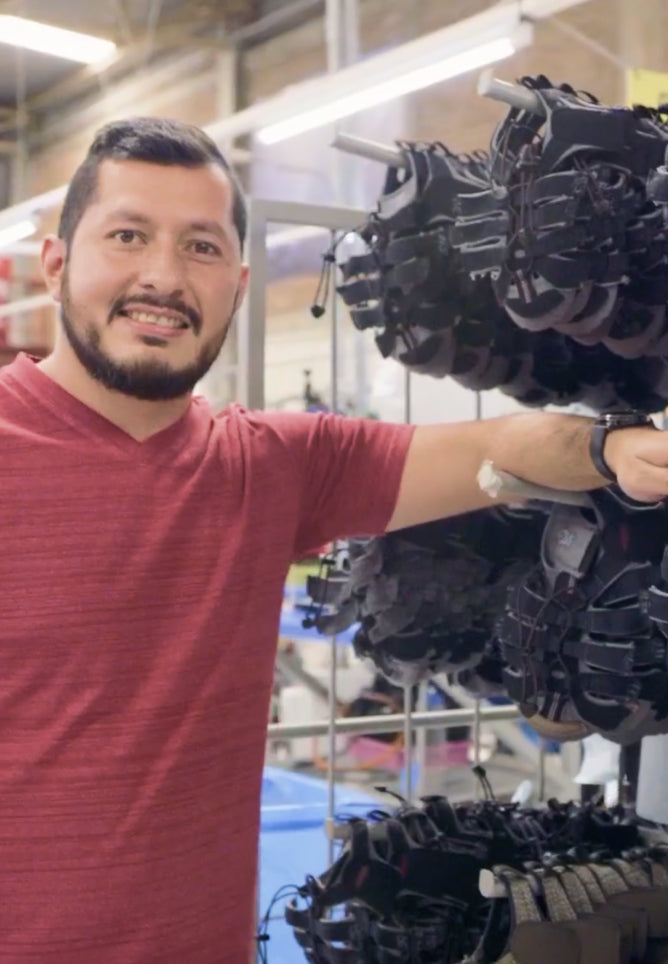 Man in red shirt standing in front of of half-made sandals in a factory