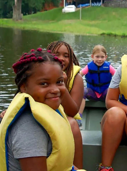 Four kids in life jackets sitting in a boat together and smiling 