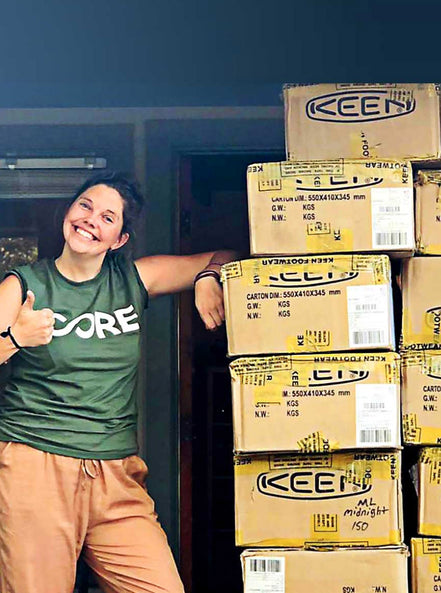 Woman standing next to pile of boxes filled with Keen shoe donations