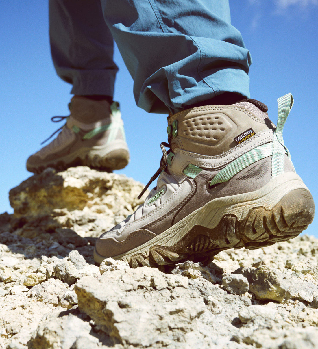 Knee down shot of woman wearing tan Targhee IV hiking boots and walking over rocky surface. 
