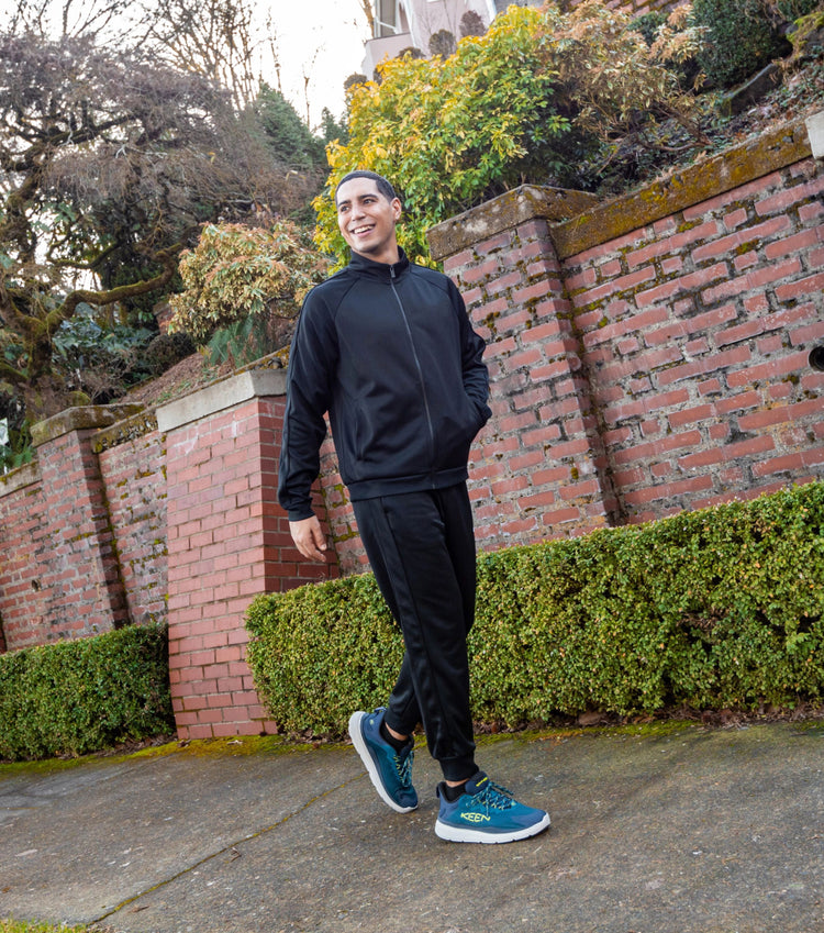Man in black tracksuit wearing bluke WK450 walking shoes and walking on neighborhood sidewalk. 