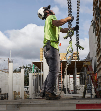 Man in construction clothing and helmet holding chain form large pulley system at construction site. 