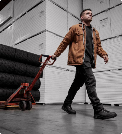 Man in warehouse pulling large cart of black rubber material while wearing black Kenton work shoes