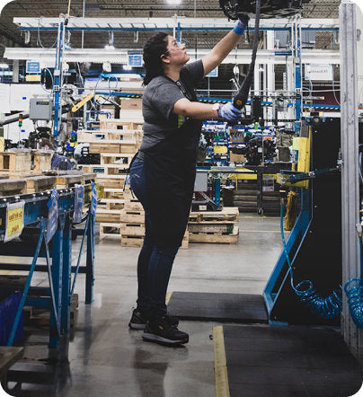 Woman wearing apron, gloves, and safety glasses working on shoe line in factory