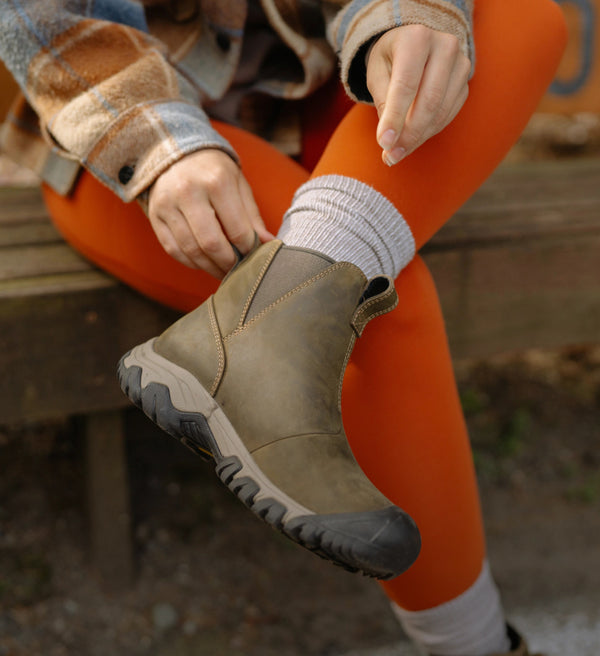 A person pulling on a pair of olive green KEEN slip-on boots.