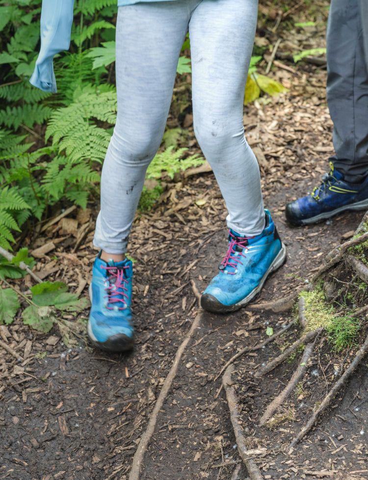 Knee down view of kids wearing wanduro shoes walking over treet roots 