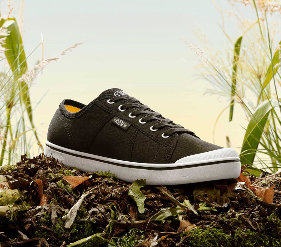 A black KEEN casual sneaker sitting on a pile of grass and dirt.