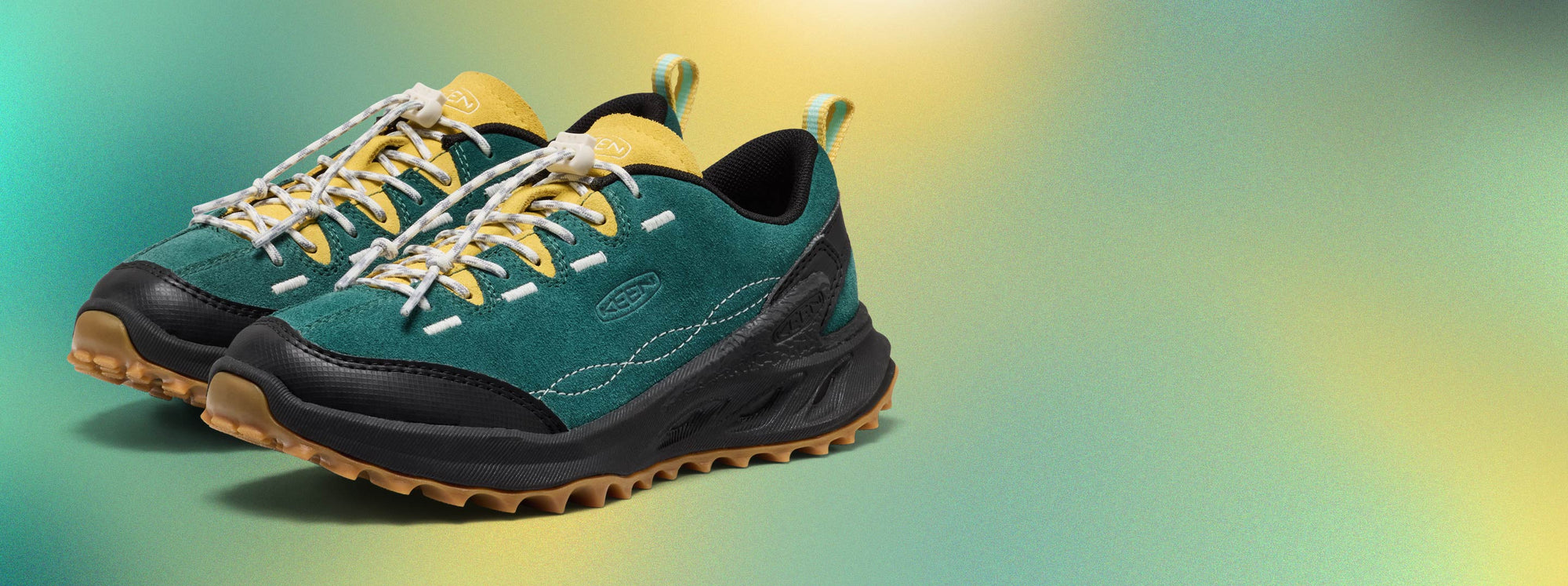 Product shot of turquoise, yellow, and black suede jasper Zionic casual sneakers with a yellow and blue gradient background. 