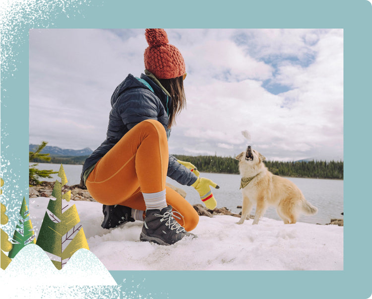 Woman wearing Revel snow boots kneelig in snow with her tan dog.