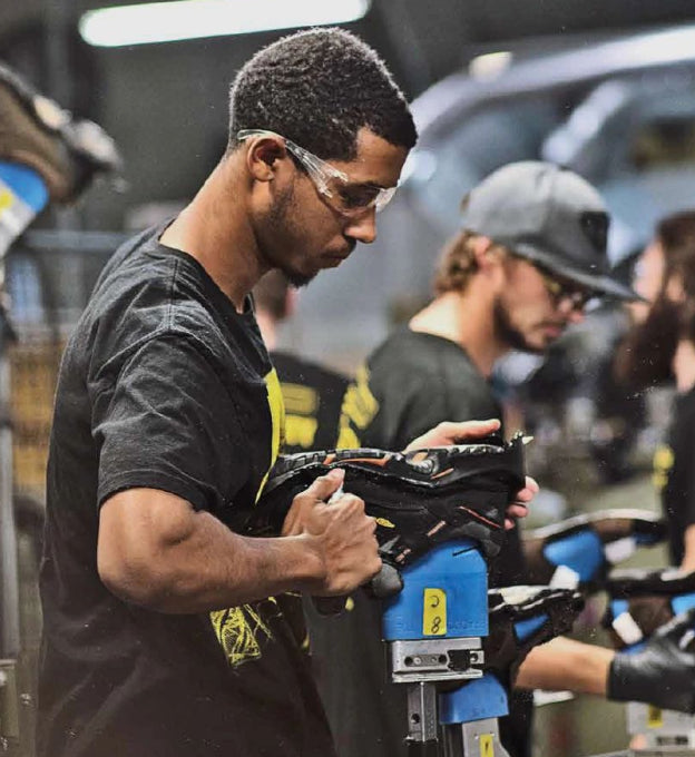 Man in safety glasses working with factory machine to attach part of a shoe. 